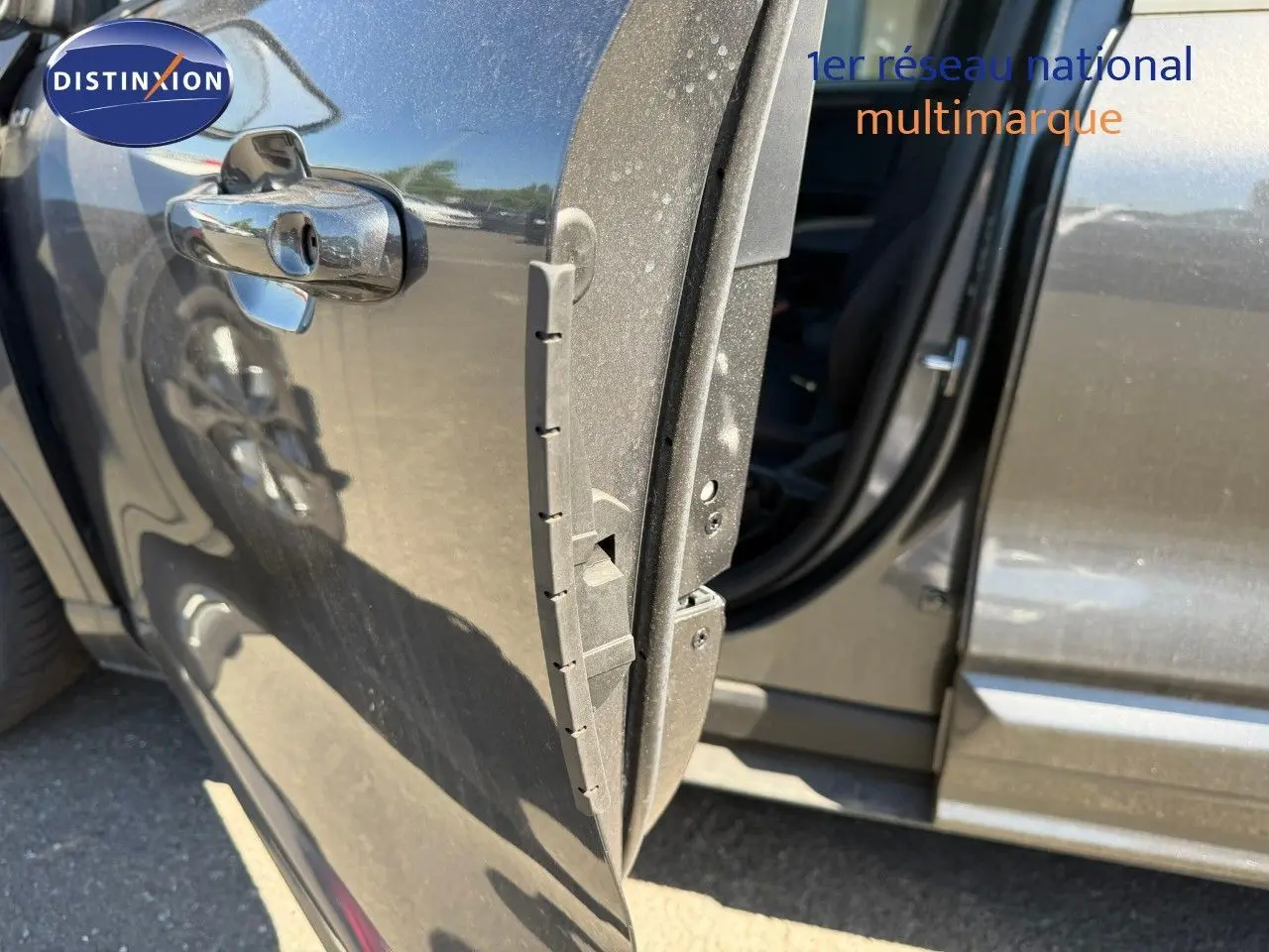 Vue rapprochée de la porte avant gauche ouverte d’un Ford Kuga 2024 gris magnétique métal, avec reflet et intérieur partiellement visible.