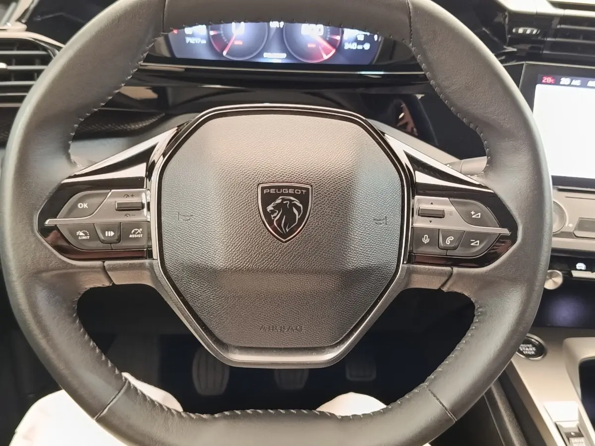 Vue rapprochée du volant cuir noir de la Peugeot 308 2023 avec commandes multifonctions et tableau de bord digital.
