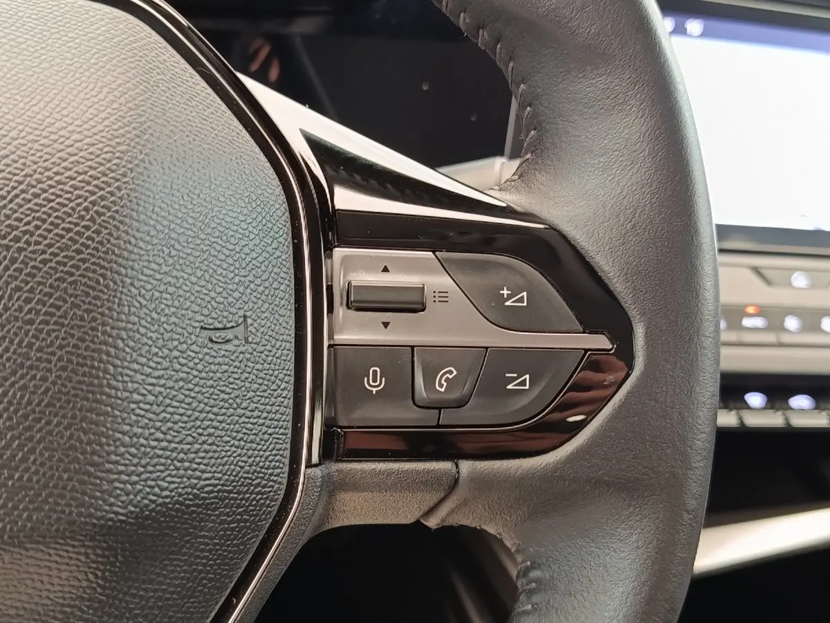 Gros plan sur les commandes du volant en cuir noir de la Peugeot 308 blanche, version PureTech 130 S&S ACTIVE PACK 2023.