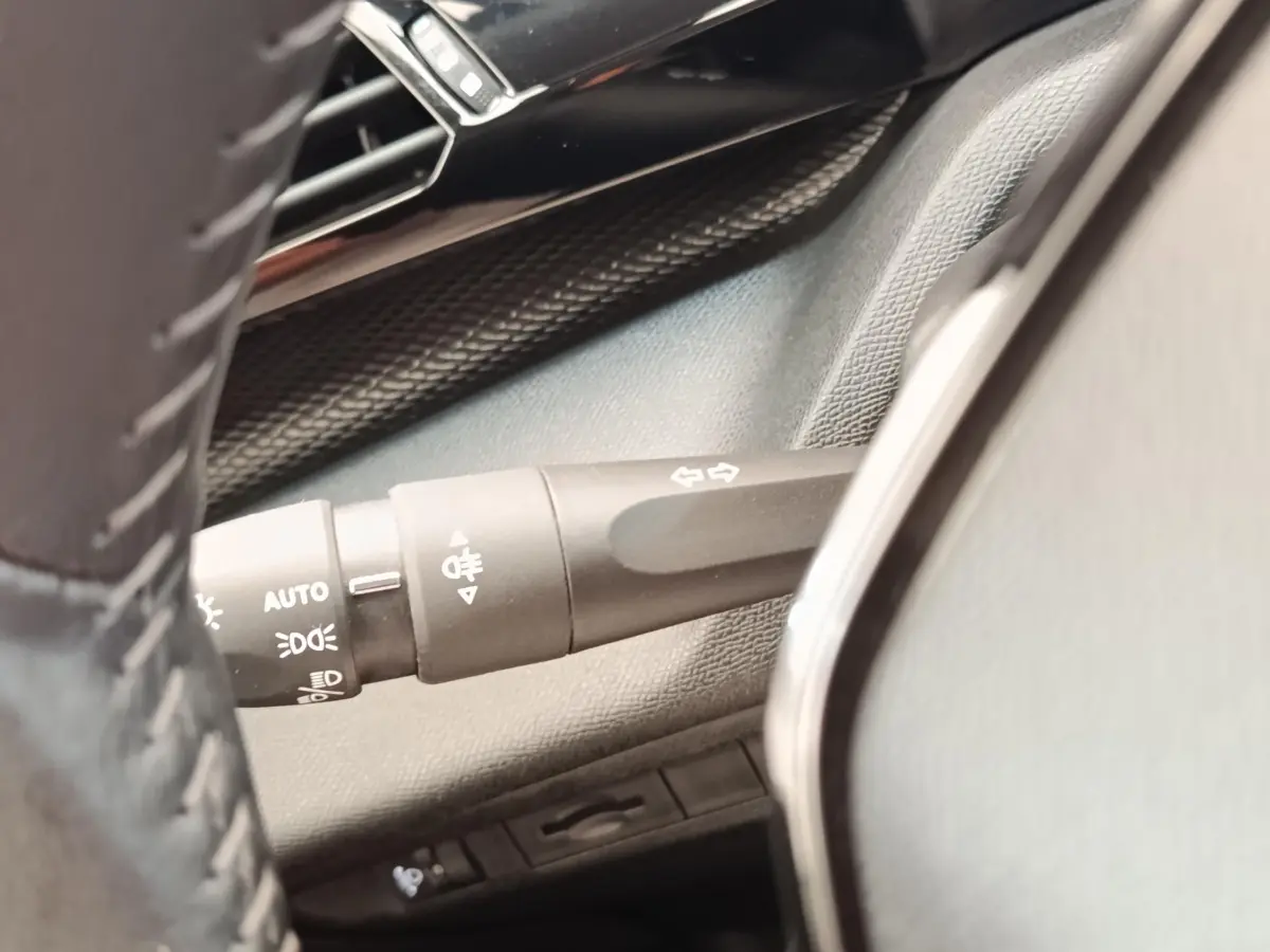 Gros plan sur la commande des clignotants et feux à gauche du volant cuir dans l’habitacle d’une Peugeot 308 blanche.