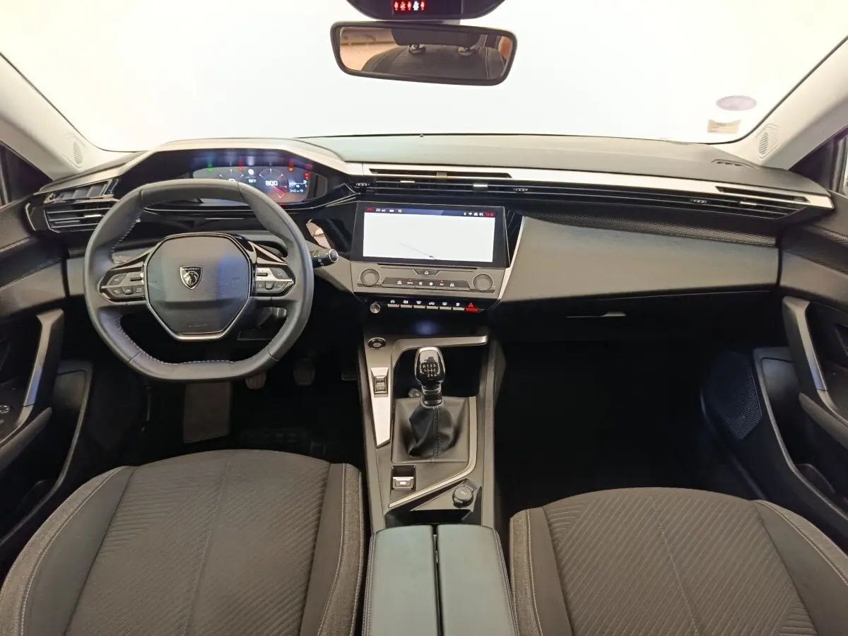 Vue intérieure avant de la Peugeot 308 2023, volant cuir, écran tactile central et levier de vitesses manuel noir.