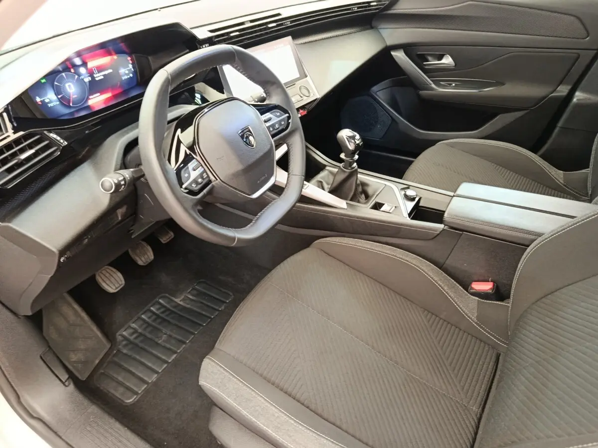 Vue intérieure côté conducteur de la Peugeot 308 PureTech 130 blanche, volant cuir et tableau de bord digital.