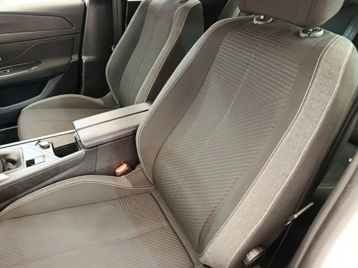 Gros plan sur les sièges avant gris foncé et la console centrale de la Peugeot 308 blanche, version 2023.