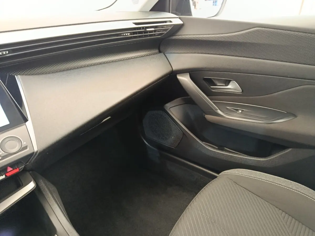 Intérieur côté passager de la Peugeot 308 blanche 2023, montrant la planche de bord et la porte en tissu noir.