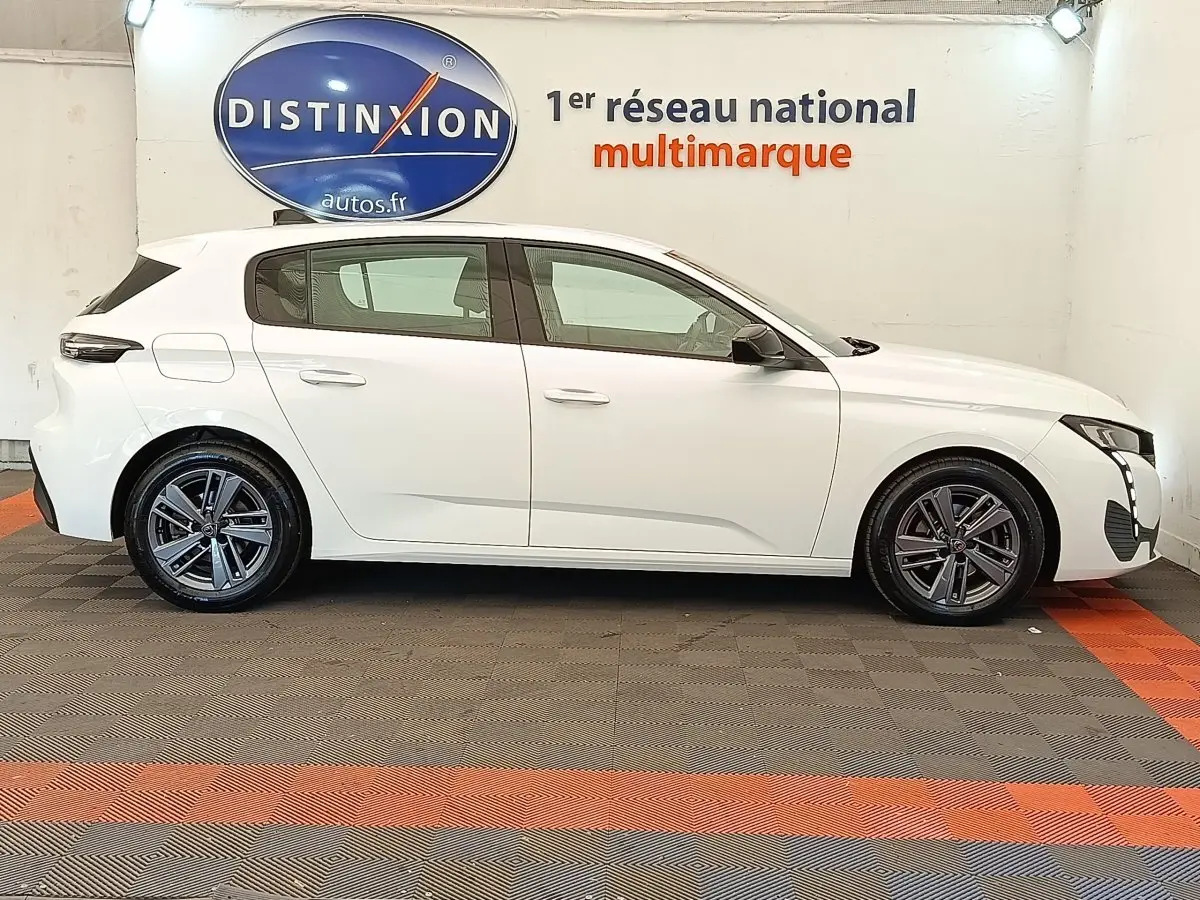 Profil droit d'une Peugeot 308 blanche 2023 avec jantes alliage et feux LED, en intérieur showroom.