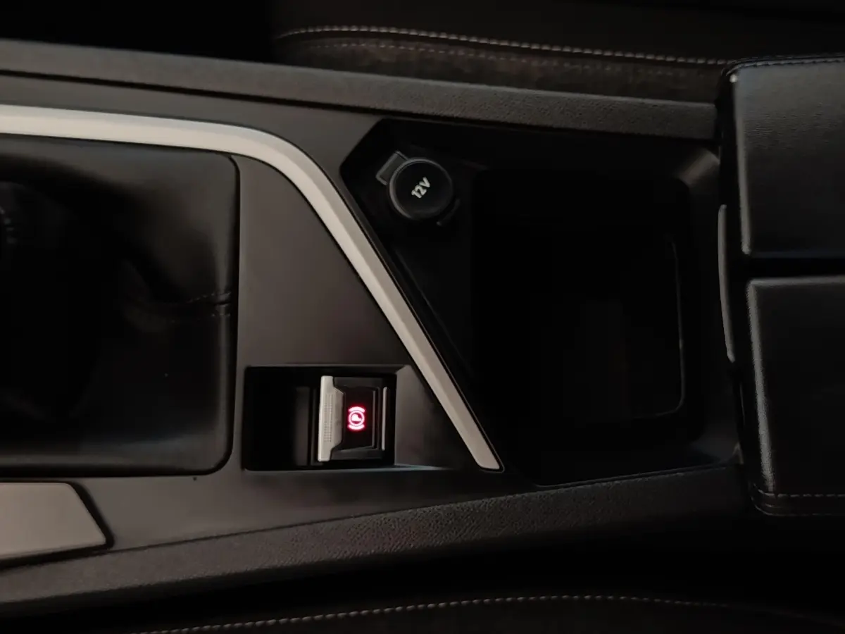Gros plan sur la console centrale noire avec frein à main électrique et prise 12V dans une Peugeot 308 blanche.