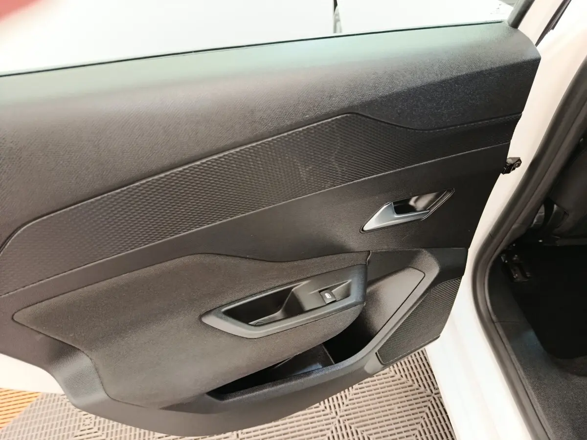 Vue intérieure côté gauche de la porte avant d'une Peugeot 308 blanche, avec panneau noir et commande de vitre.