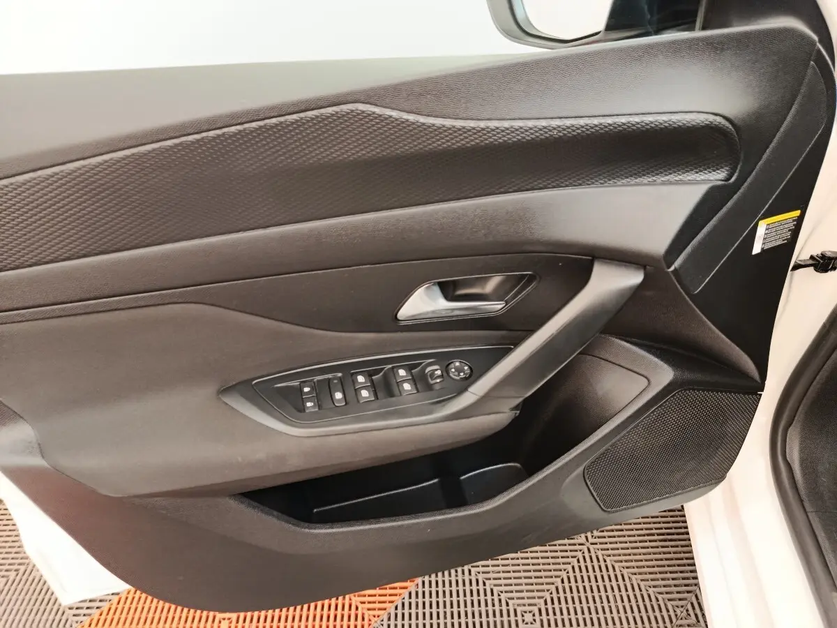 Vue intérieure côté gauche de la porte avant blanche d'une Peugeot 308 2023 avec commandes électriques et poignée argentée.