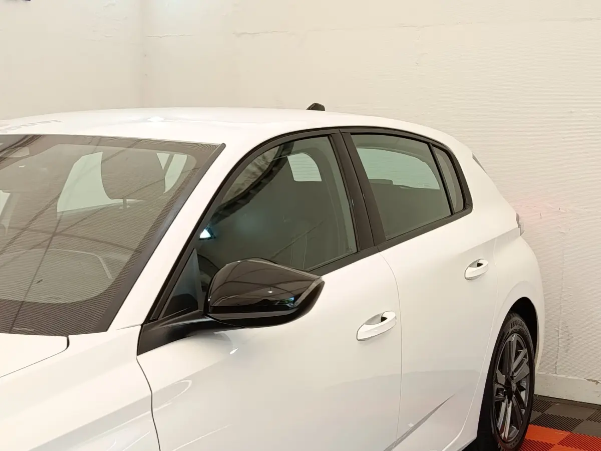 Vue côté gauche d'une Peugeot 308 blanche 2023 avec rétroviseur noir brillant et jantes alliage distinctives.