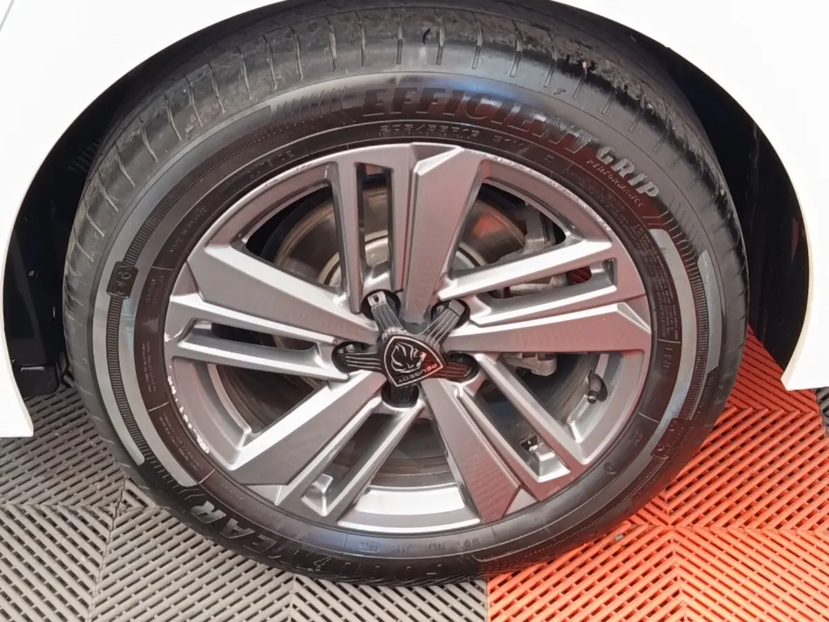 Gros plan sur la roue avant droite d'une Peugeot 308 blanche, avec jante alliage au design moderne.