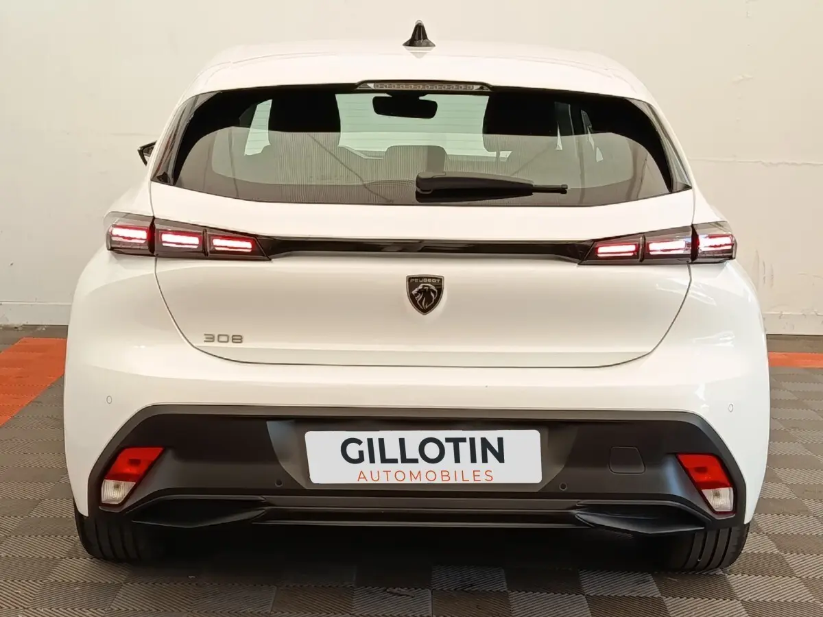 Vue arrière d'une Peugeot 308 blanche 2023 avec feux LED allumés et logo lion central sur le hayon.