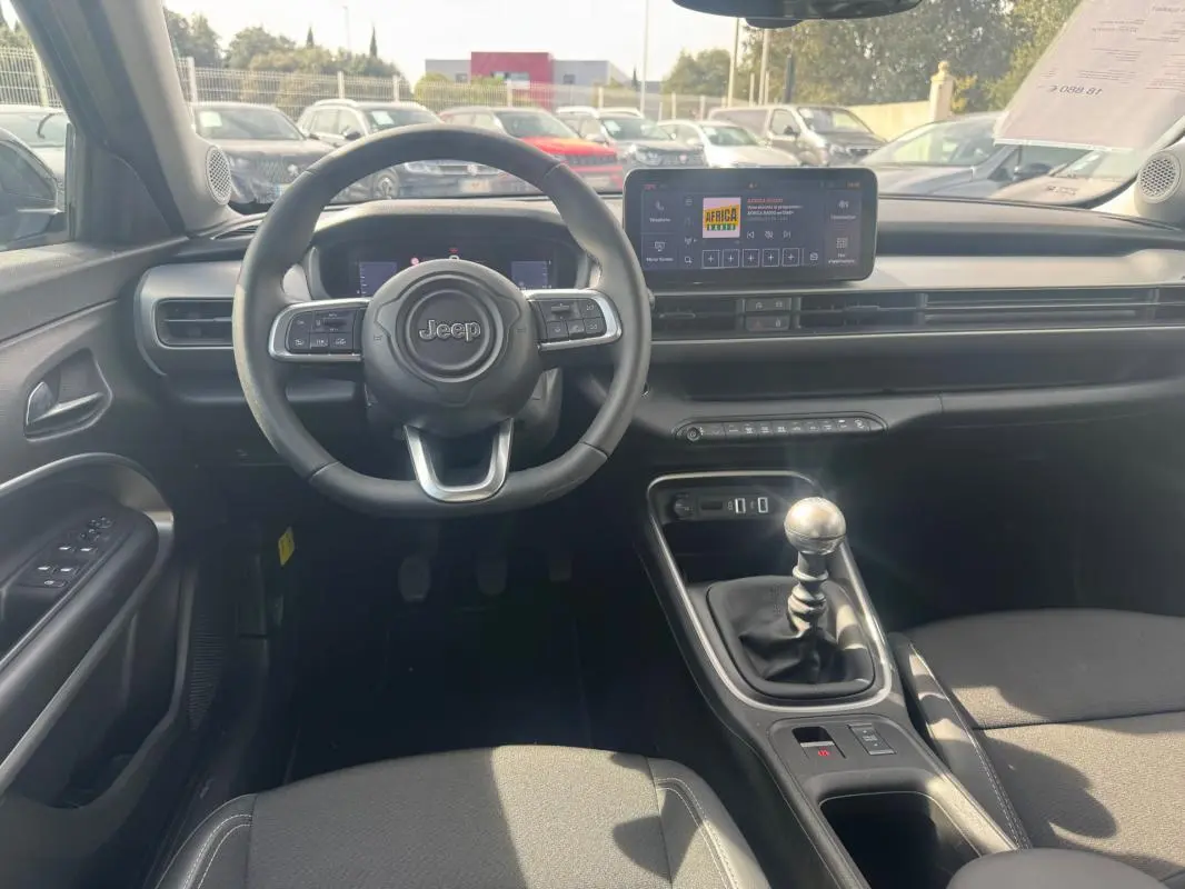 Intérieur du Jeep Avenger gris foncé vu de face, avec volant multifonction, écran tactile et levier de vitesses manuel.