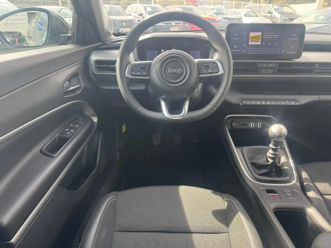 Vue intérieure frontale du Jeep Avenger 2025 gris foncé, volant multifonction et levier de vitesse manuel visibles.