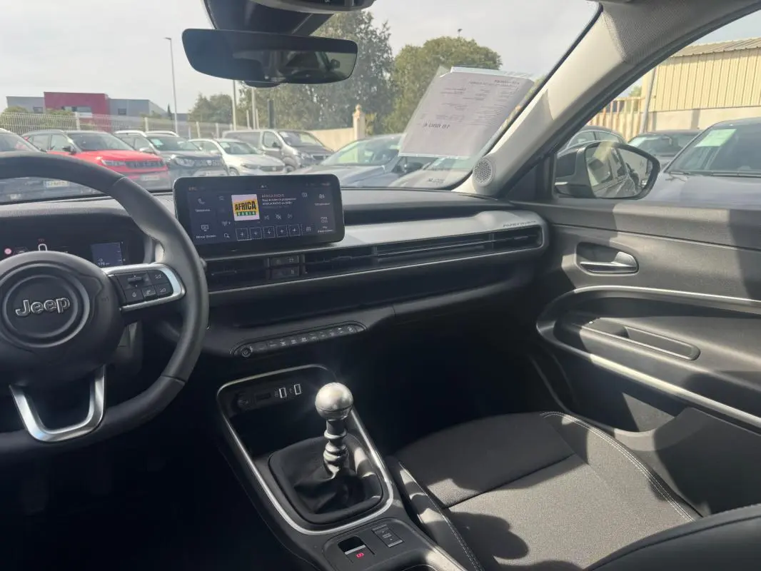 Intérieur du Jeep Avenger gris foncé vu côté conducteur, avec tableau de bord moderne et levier de vitesses manuel visible.
