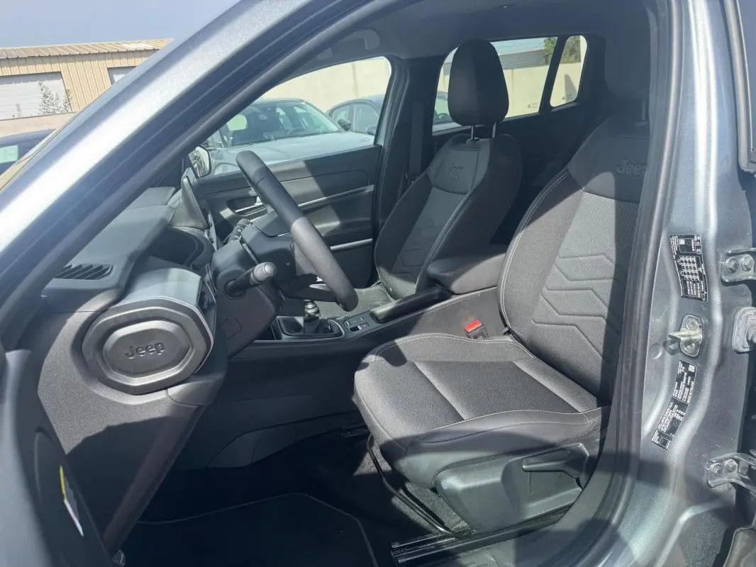 Vue intérieure côté conducteur du Jeep Avenger gris foncé 2025, montrant les sièges et la console avec boîte manuelle.