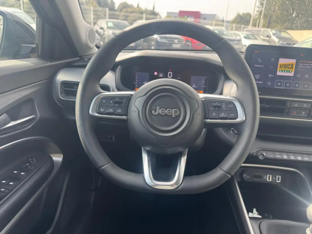 Vue intérieure centrée sur le volant Jeep noir du Jeep Avenger 2025, avec tableau de bord digital et écran tactile visible.