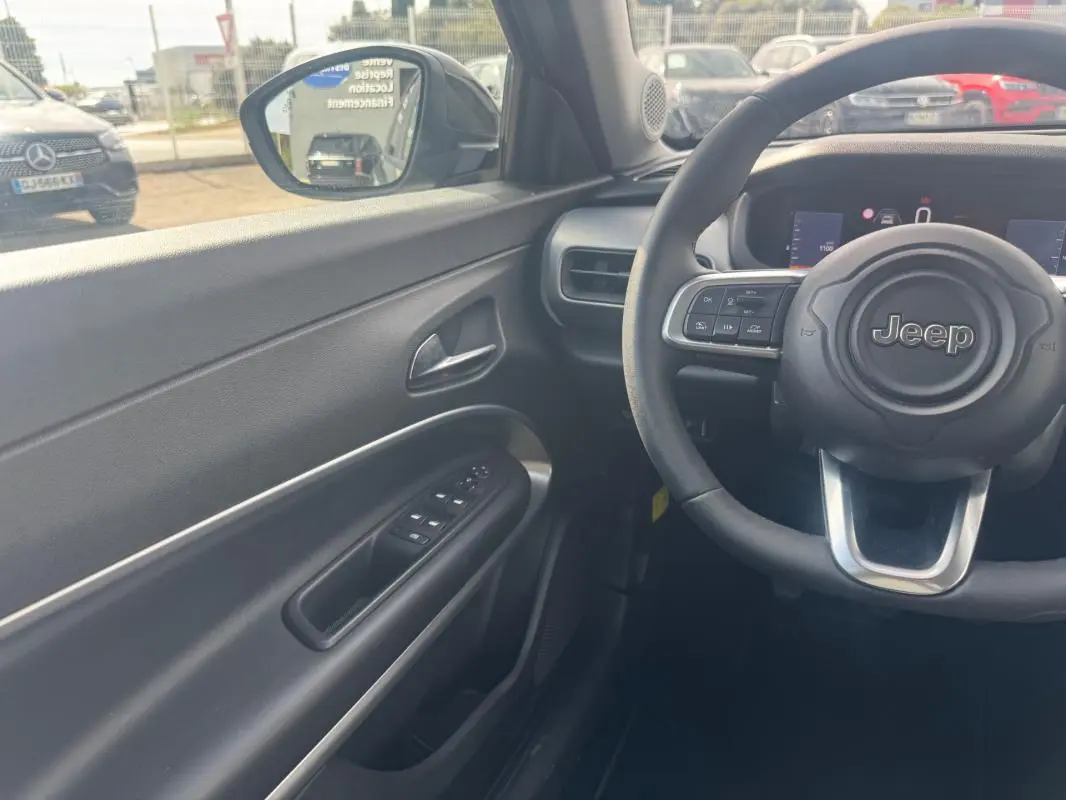 Vue intérieure côté conducteur du Jeep Avenger 2025 gris foncé, avec volant multifonctions et tableau de bord numérique.