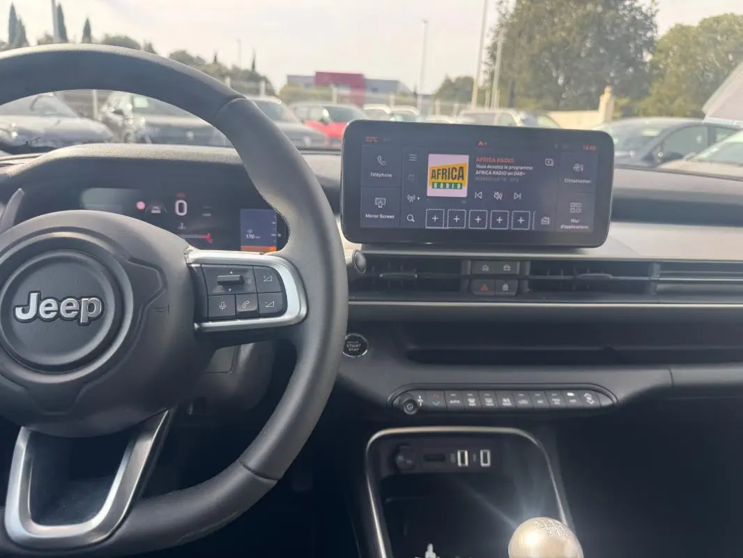Vue intérieure de face du tableau de bord gris foncé du Jeep Avenger 2025 avec volant, écran tactile et levier de vitesse manuel.