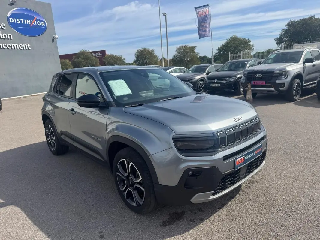 Jeep Avenger gris foncé vu en 3/4 avant droit sur parking, avec calandre distinctive et jantes noires et argentées.