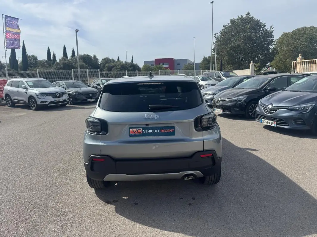 Vue arrière d'un Jeep Avenger gris foncé 2025, avec feux arrière fumés et plaque V.O. Véhicule récent visible en parking.