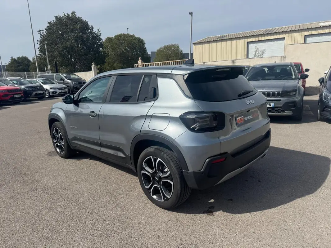 Jeep Avenger gris foncé vue 3/4 arrière droit, avec jantes spécifiques et vitres arrière teintées, stationné en extérieur.