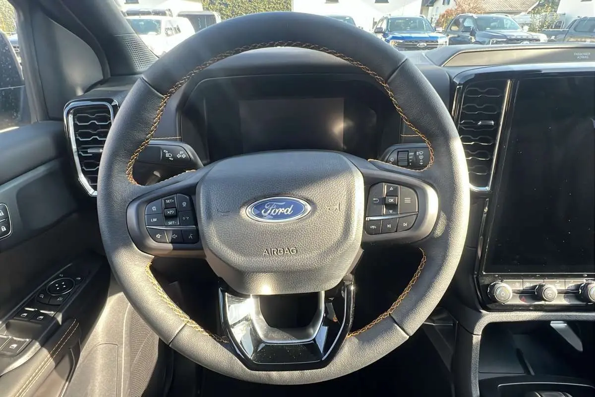 Vue rapprochée du volant cuir noir avec surpiqûres marron du Ford Ranger 2026, tableau de bord et écran tactile visibles.