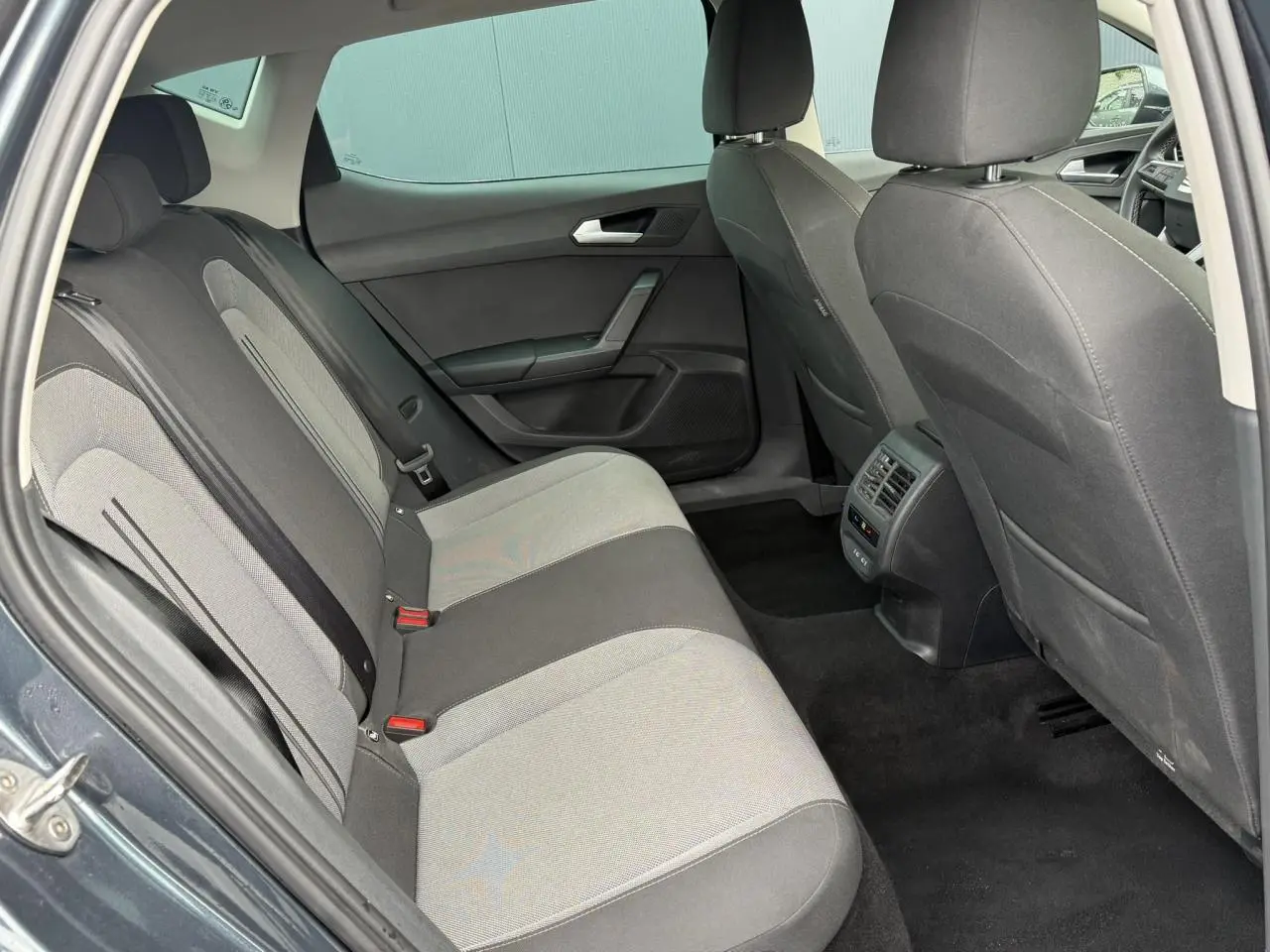 Vue intérieure arrière côté gauche du SEAT Leon 2025, montrant les sièges tissu bicolores et les vitres surteintées.