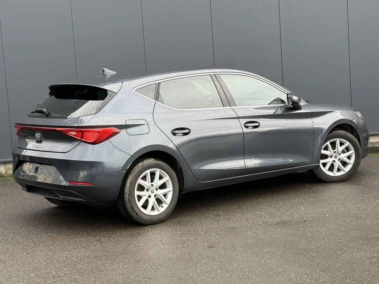 SEAT Leon 1.5 TSI 115 Style gris magnétique vue de profil côté droit sur sol humide devant un mur gris.