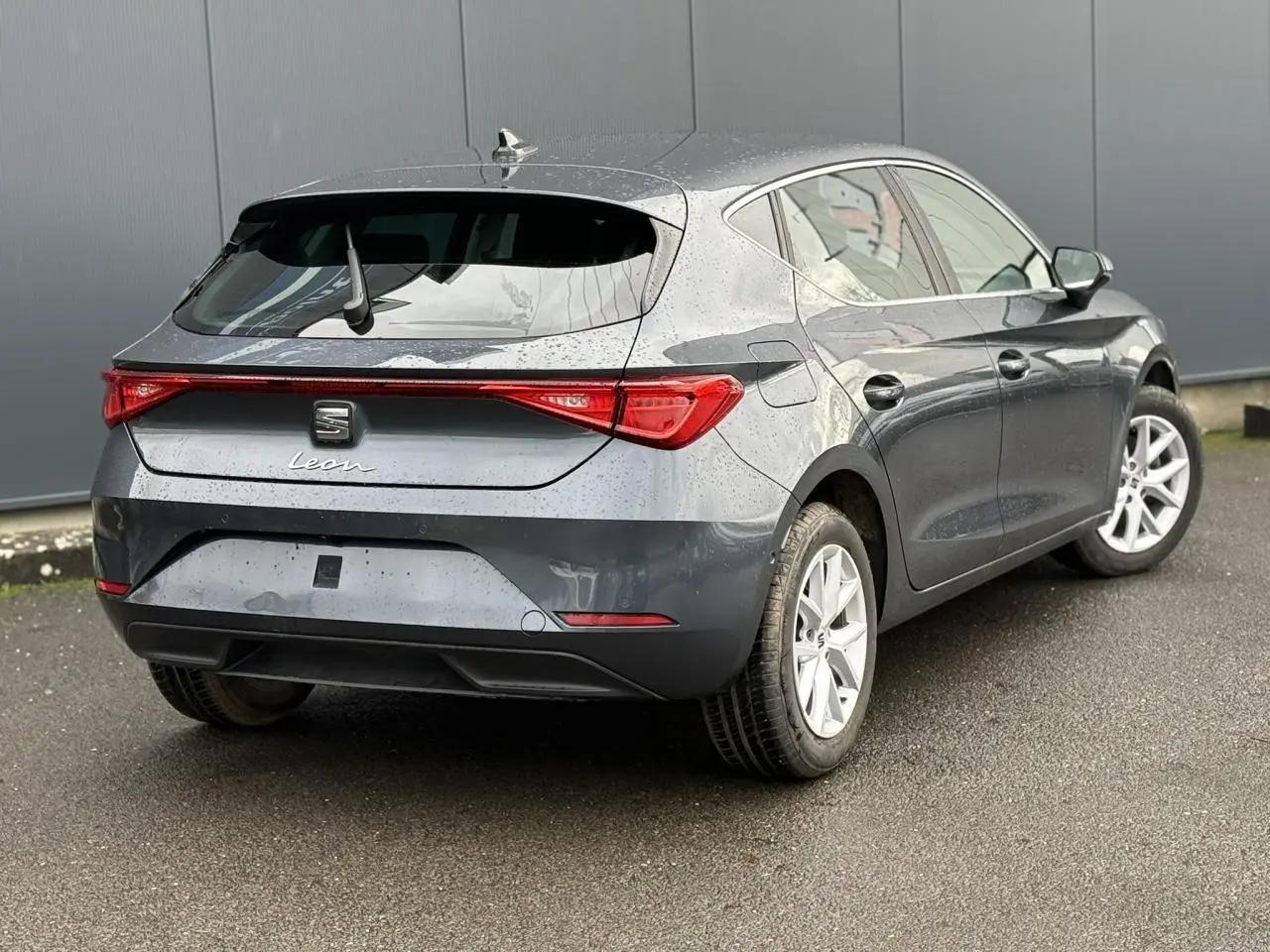 Vue 3/4 arrière droite d'une SEAT Leon 1.5 TSI 115 Style gris magnétique avec jantes alliage 16 pouces sur sol humide.