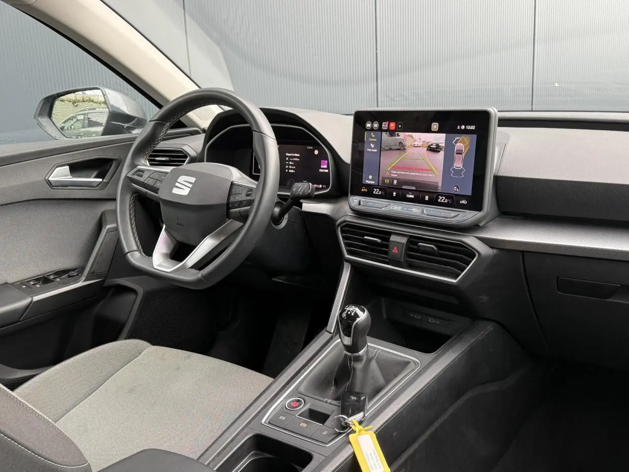 Vue intérieure côté conducteur du SEAT Leon 1.5 TSI gris, avec volant cuir multifonction et écran tactile affichant la caméra de recul.