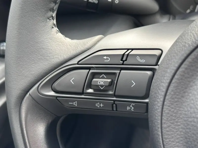 Gros plan sur les commandes multifonctions noires du volant cuir de la Toyota Yaris blanche, version 116h Dynamic 2025.