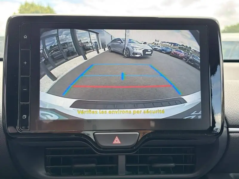 Écran tactile montrant la caméra de recul d’une Toyota Yaris blanche, vue arrière avec lignes de guidage colorées.