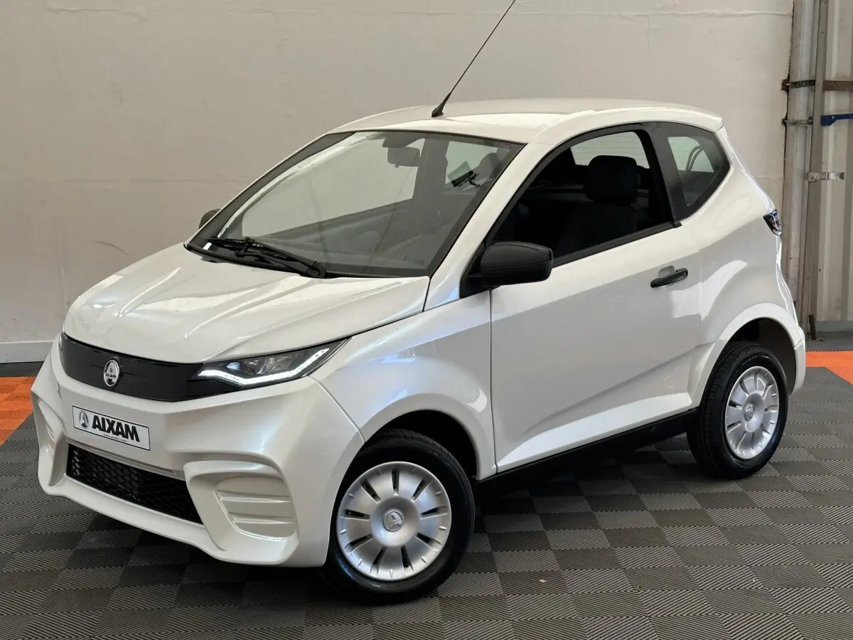 Vue 3/4 avant droite de l'AIXAM AMBITION 0.5 CITY PACK blanche, avec rétroviseur caméra côté conducteur visible.