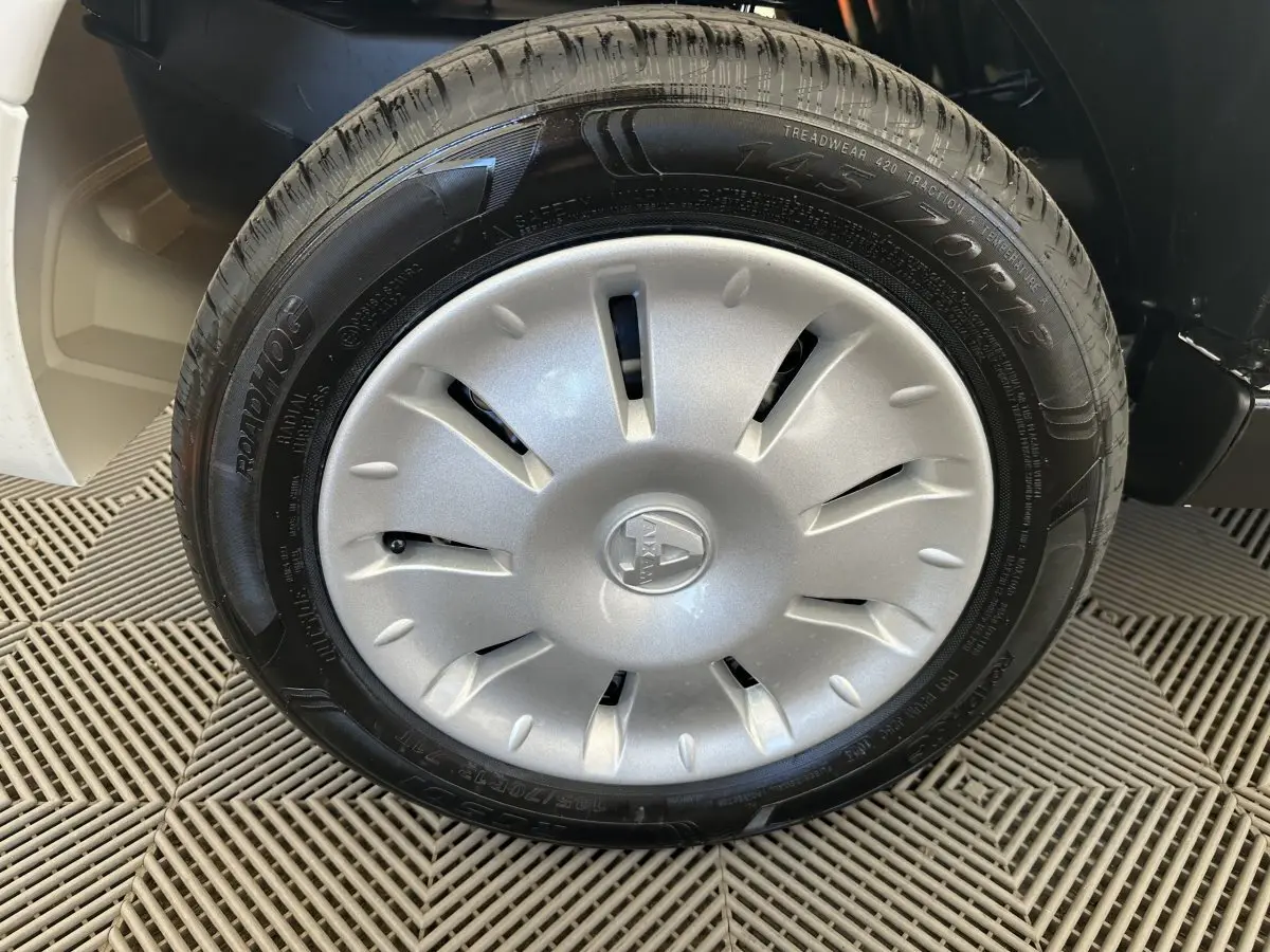 Gros plan sur la roue avant droite d'une Aixam Ambition blanche, avec enjoliveur argenté et logo central visible.