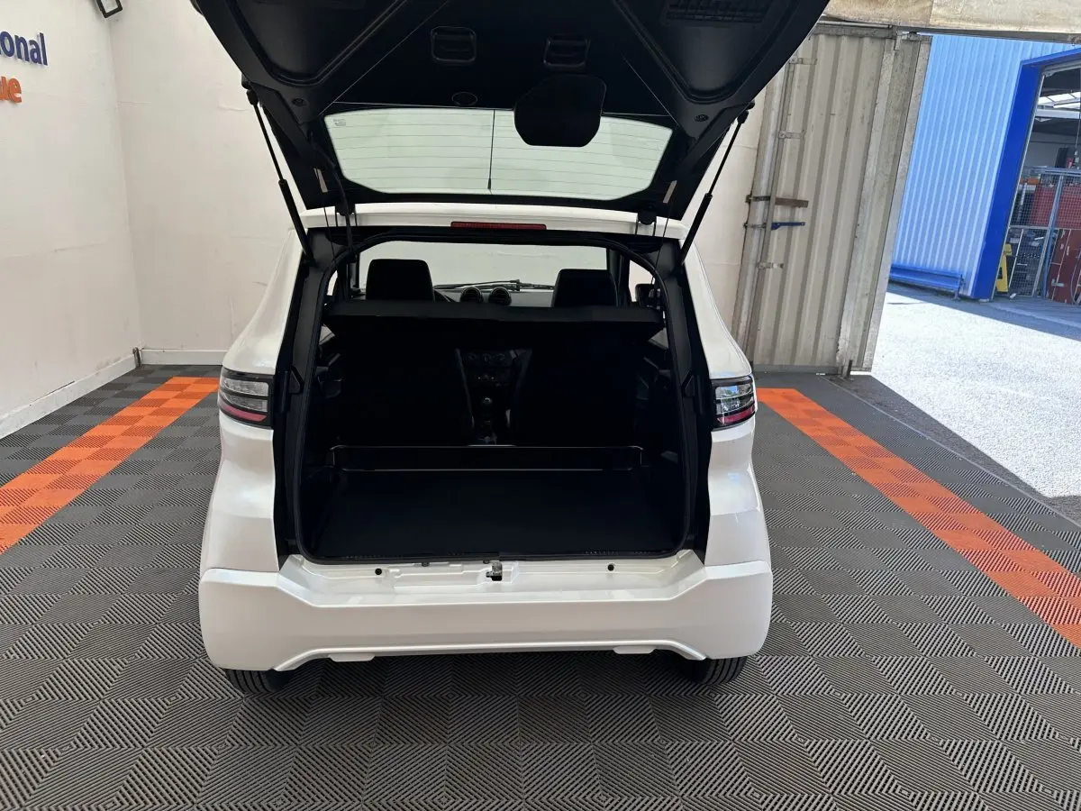 Vue arrière d'une Aixam Ambition 0.5 City Pack blanche avec coffre ouvert, montrant l'intérieur et l'habitacle.