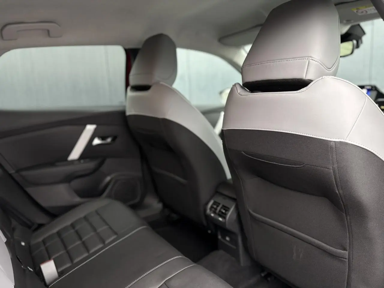 Vue intérieure arrière côté gauche de la Citroën C4 Hybrid 2025, sièges bicolores gris clair et noir avec surpiqûres blanches.