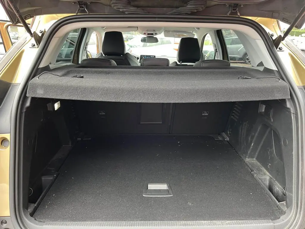 Coffre ouvert vu de l'arrière d'un Peugeot 3008 jaune clair, avec cache-bagages et sièges arrière visibles.