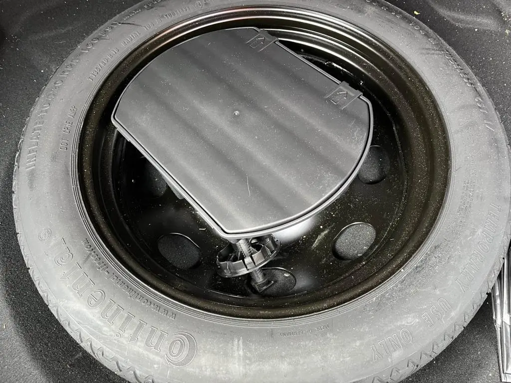 Roue de secours noire montée sur jante acier, visible dans le coffre d’un Peugeot 3008 jaune clair.