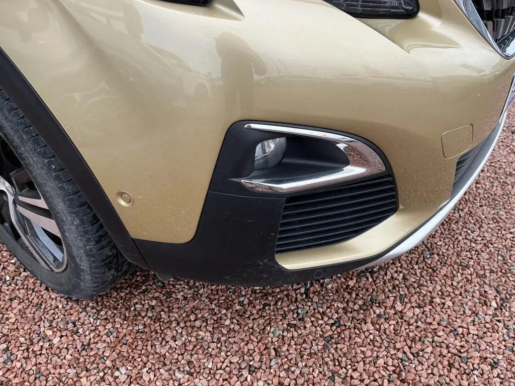 Gros plan sur le pare-chocs avant droit jaune clair du Peugeot 3008 avec antibrouillard et capteur de stationnement.