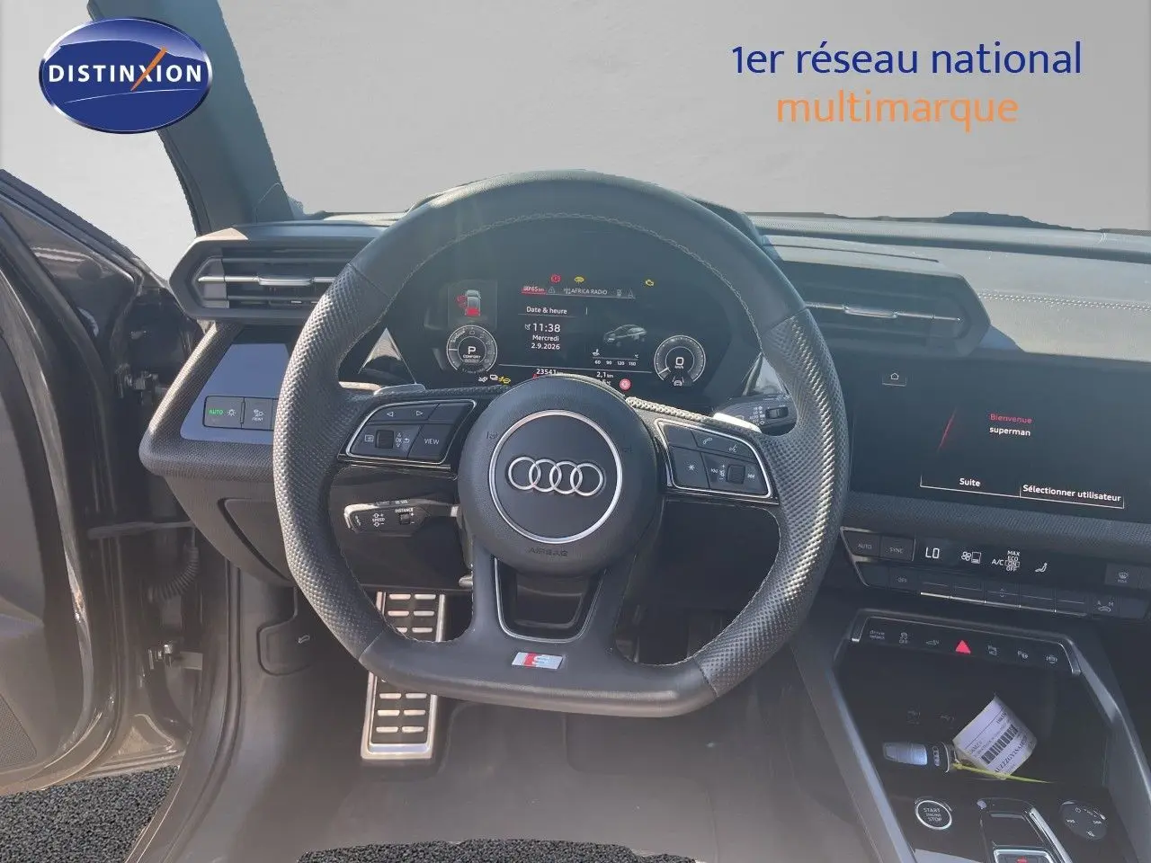 Vue intérieure centrée sur le volant sport Audi A3 Sportback gris Daytona, tableau de bord numérique et écran tactile visibles.