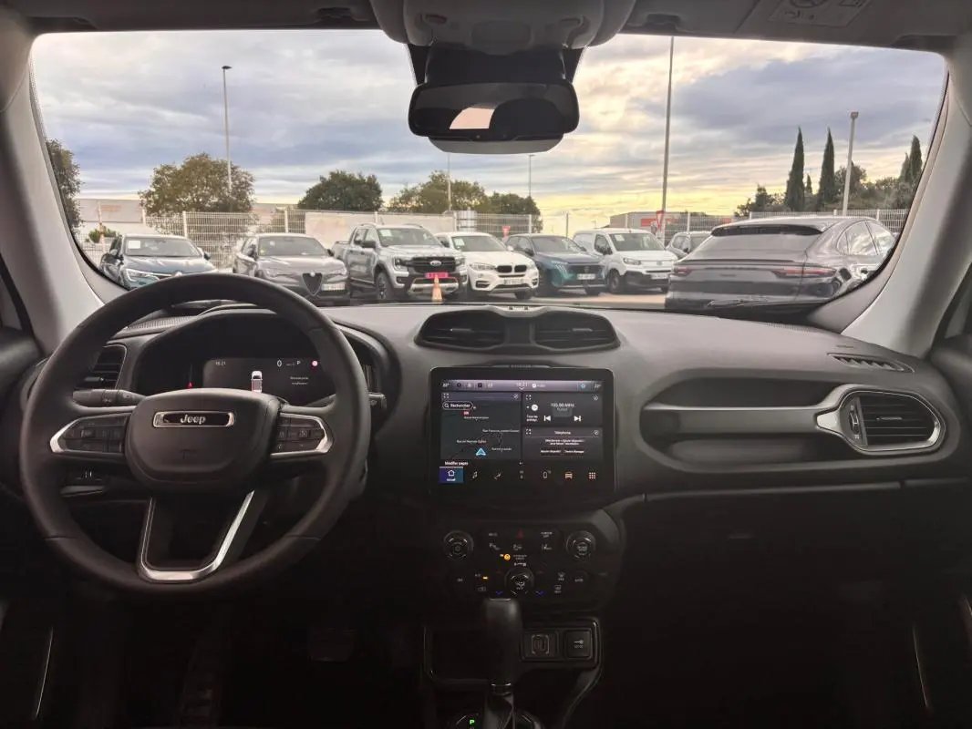 Vue intérieure frontale du tableau de bord du Jeep Renegade 2024 blanc, avec écran tactile central et volant multifonction.