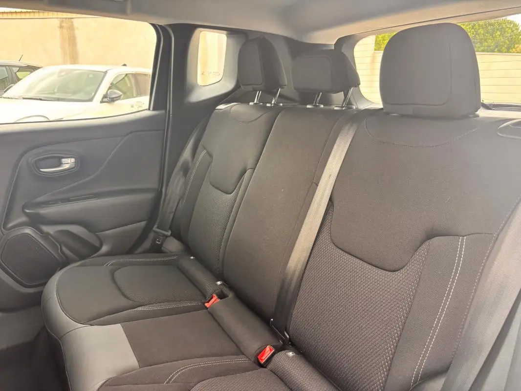 Vue intérieure arrière côté gauche du Jeep Renegade 2024 blanc, sièges tissu noir avec ceintures de sécurité visibles.
