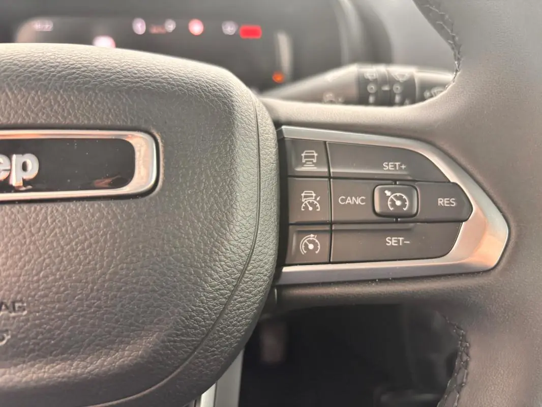 Gros plan sur les commandes de régulateur de vitesse au volant noir du Jeep Renegade 2024 blanc e-Hybrid Altitude.