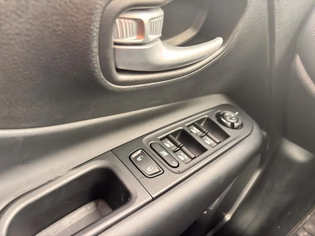 Gros plan sur la commande des vitres et la poignée intérieure côté conducteur d'une Jeep Renegade 2024 noire.