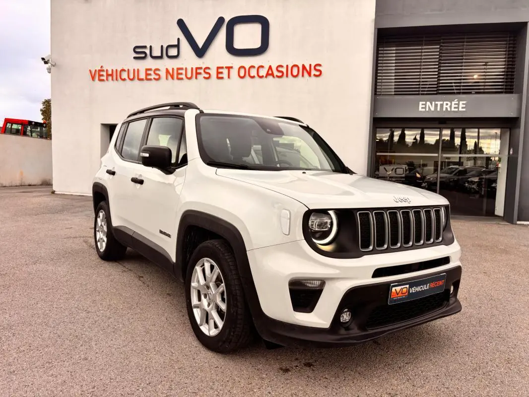 Vue 3/4 avant droite d’un Jeep Renegade blanc 2024 avec calandre noire et jantes argentées, devant un showroom.