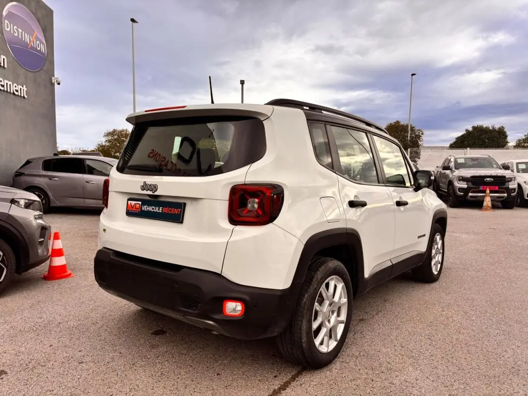 Vue 3/4 arrière droite d'un Jeep Renegade blanc 2024 avec feux arrière carrés et protections noires sur pare-chocs.