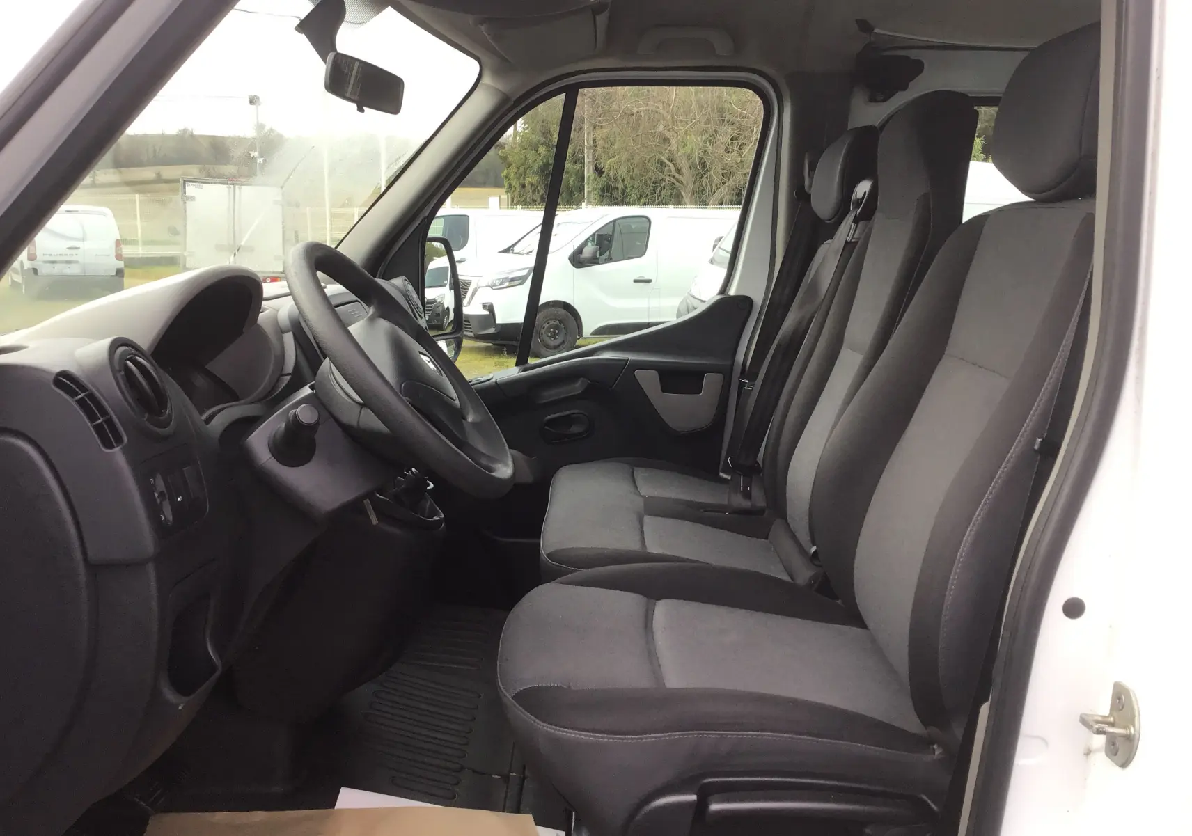 Vue intérieure côté conducteur du Renault Master Combi III blanc, montrant les sièges avant gris et le tableau de bord simple.