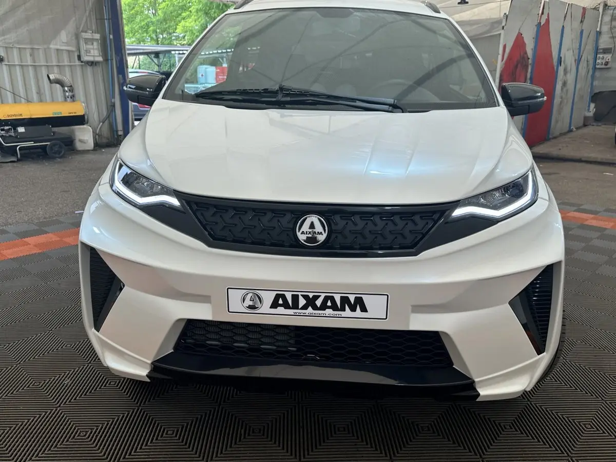 Vue de face de l'AIXAM AMBITION 0.5 CROSSOVER PREMIUM blanc avec calandre noire et rétroviseur caméra côté gauche.