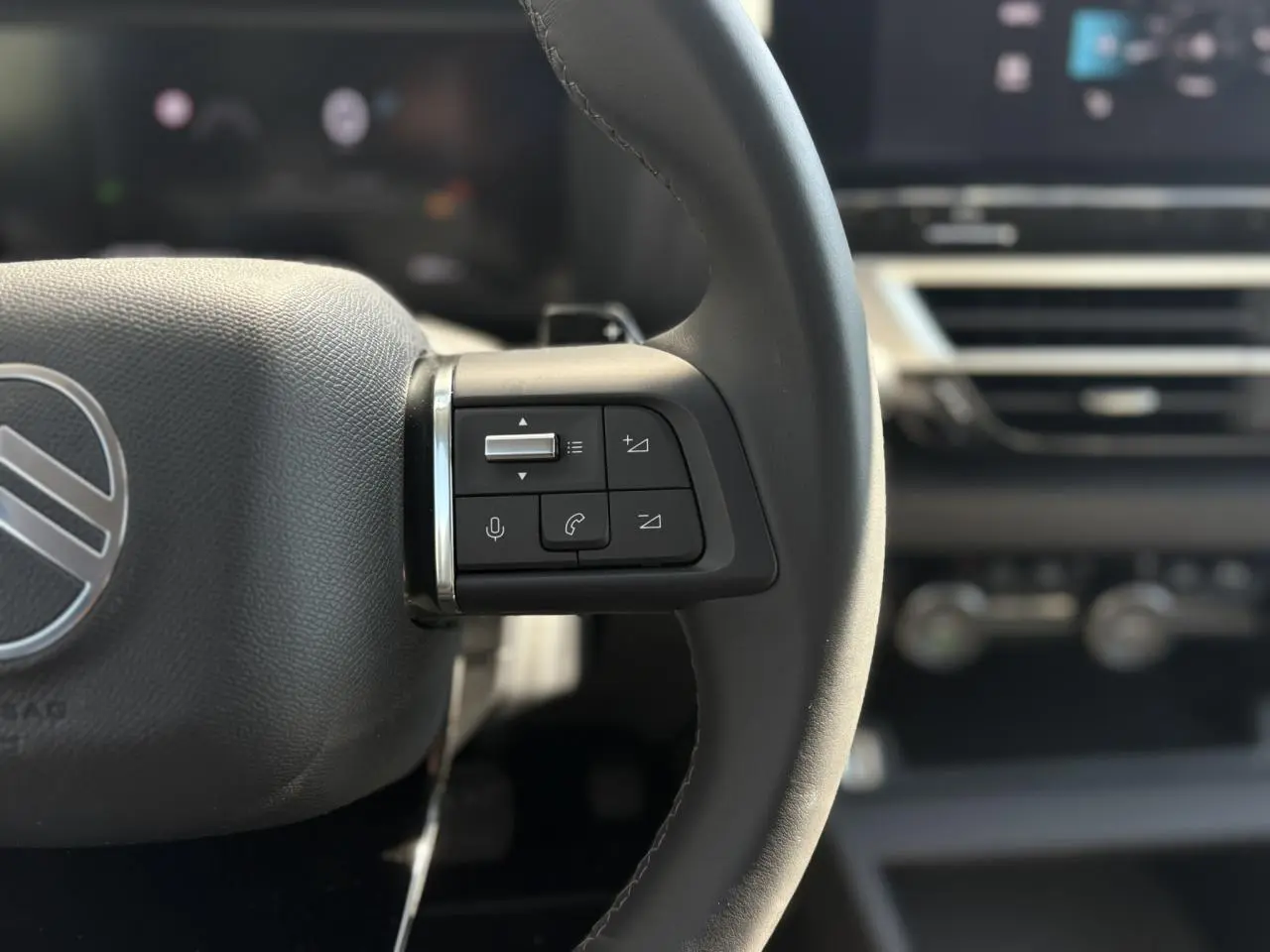 Gros plan sur les commandes gauche du volant cuir du Citroën C4 Hybrid blanc, avec tableau de bord flou en arrière-plan.