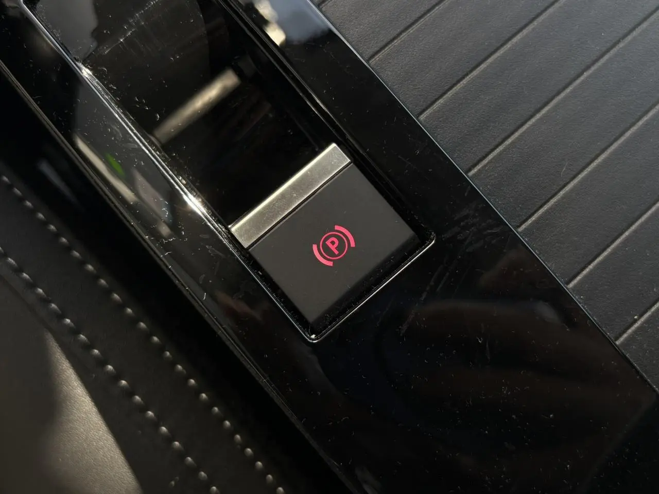 Gros plan sur le bouton de frein de stationnement électrique rouge sur console noire brillante d’une Citroën C4 Hybrid 2025.